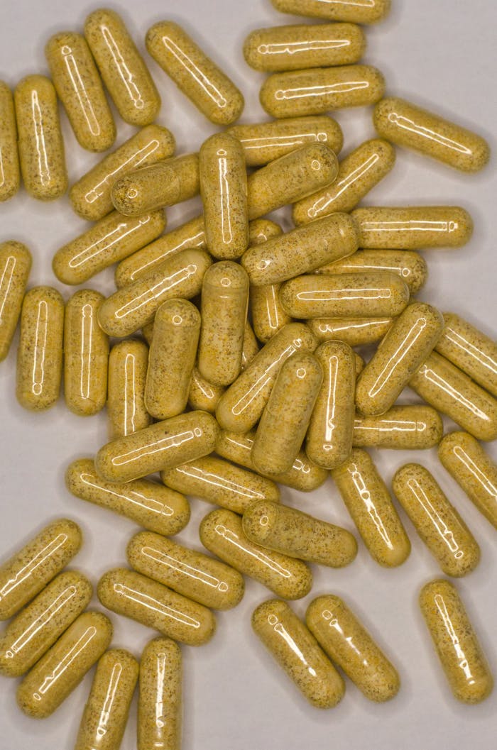 A top view of numerous herbal capsules on a gray surface, representing natural healthcare remedies.